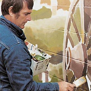 Person painting a mural on wall.